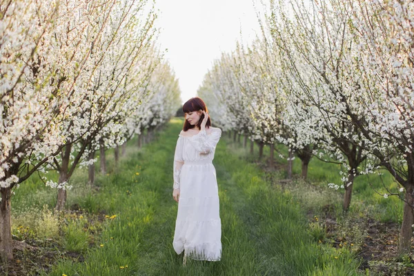 Mulher deslumbrante em vestido branco em pé no jardim da primavera — Fotografia de Stock