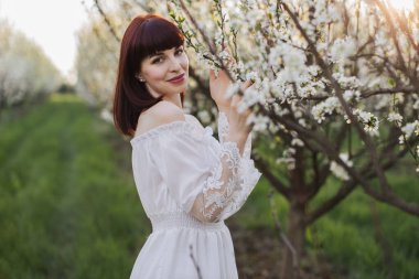 Beyaz tenli kadın çiçek açan elma ağacının yanında poz veriyor.