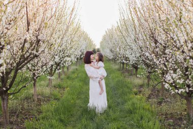 Güzel anne, bahar bahçesinde poz veriyor, elinde kızıyla.