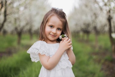 Bahar bahçesinde poz veren beyaz elbiseli güzel bir bayan çocuk.