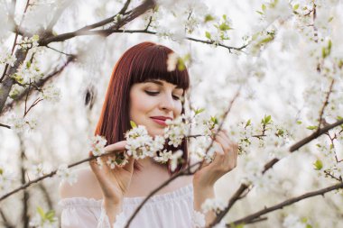 Beyaz elbiseli güzel bayan çiçeklerle dolu bahçede vakit geçiriyor.