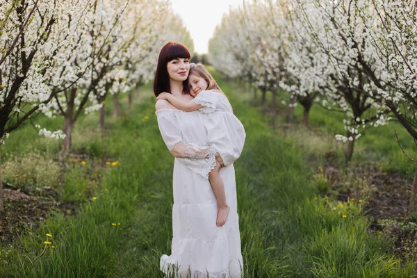 Madre sosteniendo a su hija mientras posa entre el jardín de primavera —  Fotos de Stock
