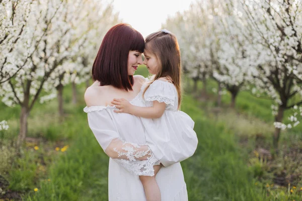 Мати тримає на руках милу дочку серед квітучого саду — стокове фото