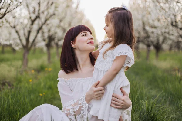 Mãe carinhosa abraçando com a filha no pomar florescendo. — Fotografia de Stock