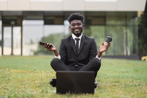 Homme d'affaires afro-américain en costume formel noir, relaxant en position lotus, assis à l'extérieur — Photo