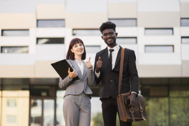 Çok ırklı iş ortakları, modern kongre merkezinin dışında duruyor ve başparmaklarını gösteriyorlar.