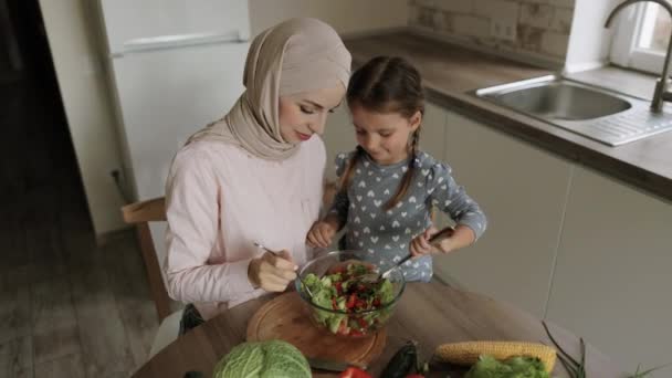 Arap kadın anne, Kafkasyalı küçük şirin kıza sağlıklı vejetaryen yemekleri yapmayı öğretiyor. — Stok video