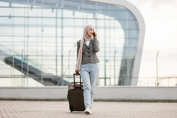 Mujer musulmana en hiyab, caminando al aire libre llevando una maleta y hablando por teléfono —  Fotos de Stock