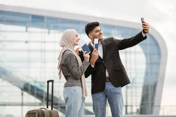 Pareja musulmana alegre, tomando selfie al aire libre cerca de la terminal del aeropuerto, sonrisa feliz y gesto —  Fotos de Stock
