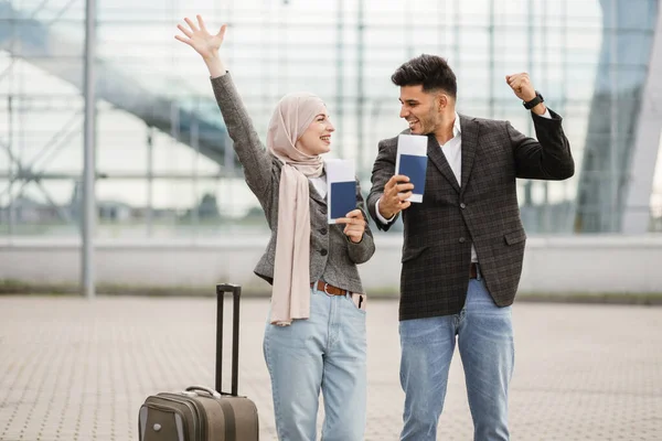 Pareja musulmana, posando en cámara afuera del aeropuerto, demostrando sus pasaportes y boletos —  Fotos de Stock