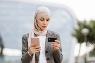 Müslüman iş kadını sokakta duruyor ve kredi kartıyla alışveriş yapıyor.