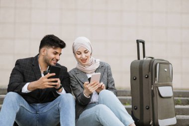 Neşeli, sırıtan iş adamı ve tesettürlü kadın merdivenlerde oturuyor.