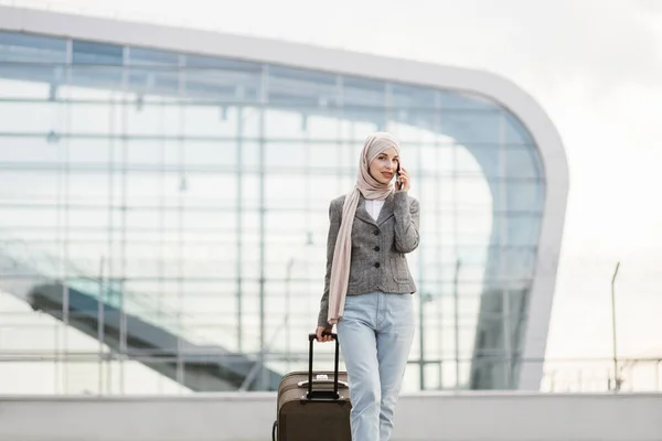 Bastante viajero turista árabe mujer en hijab llevando maleta y hablando de teléfono —  Fotos de Stock