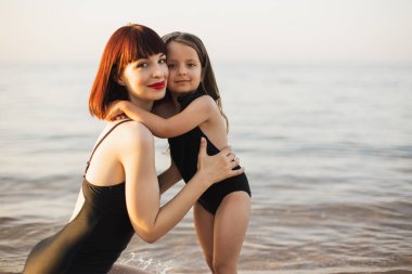 Mutlu aile gün batımında sahilde. Genç anne kızına sarılıyor..