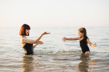 Anne ve siyah mayo giymiş kızları birbirlerine su sıçratıyorlar..