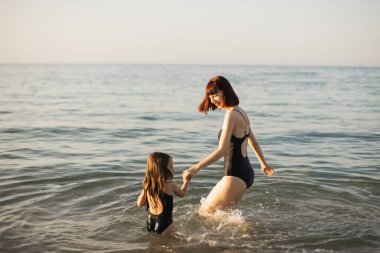 Çekici genç anne ve küçük kızı kumsalda koşuyor, gülüyor ve oynuyor..