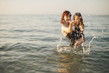 Anne ve siyah mayo giymiş kızları birbirlerine su sıçratıyorlar..