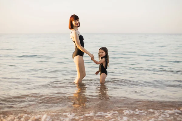 Madri mano condurre la sua bambina in costumi da bagno neri in spiaggia. — Foto Stock