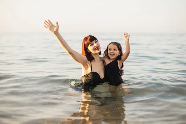 Felice mamma con piccola figlia carina nuotare nel mare blu al tramonto. — Foto Stock