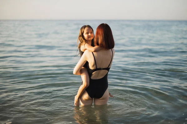 Giovane madre abbraccia e tiene tra le braccia sua figlia, godendo in bella spiaggia tropicale soleggiata. — Foto Stock