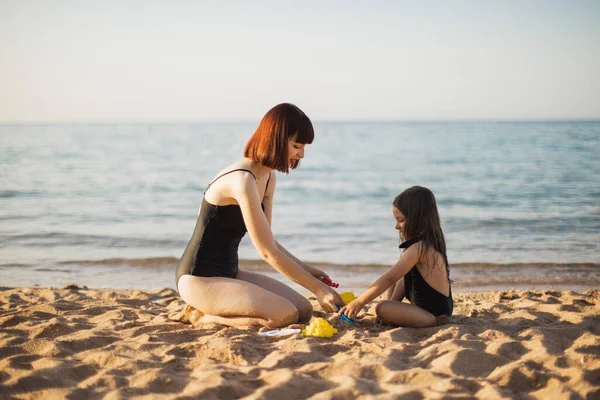 Carino bambina che gioca con la madre mentre seduto sulla riva del mare sulla spiaggia tropicale. — Foto Stock