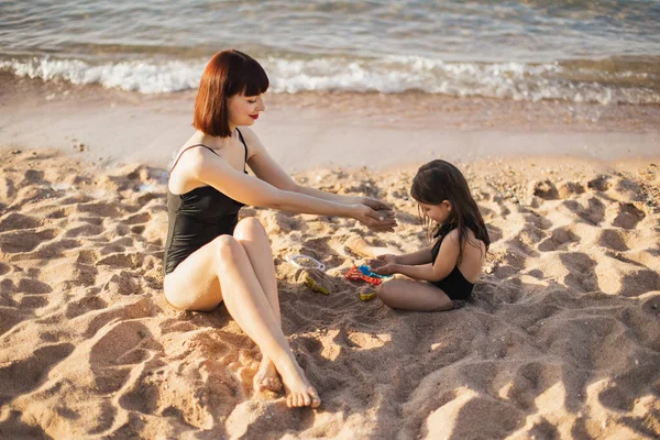 Carino bambine che giocano con la sabbia sulla spiaggia, e la mamma guardando delicatamente sua figlia. — Foto Stock