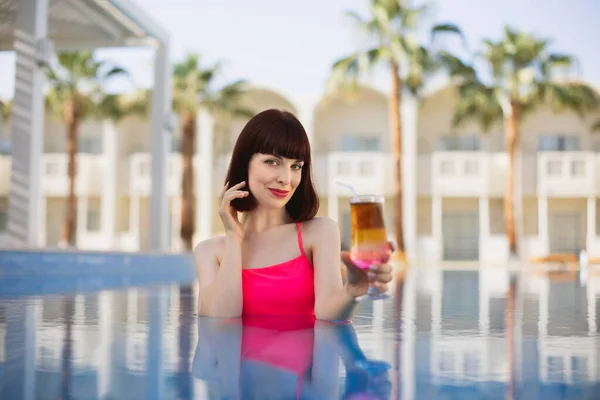 Kaukasische Frau in rosafarbener Badebekleidung entspannt sich im Schwimmbad mit Cocktail-Drink — Stockfoto