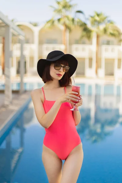 Nő divatos rózsaszín fürdőruhában, ül a medence mellett koktéllal és élvezi a nyári napot. — Stock Fotó