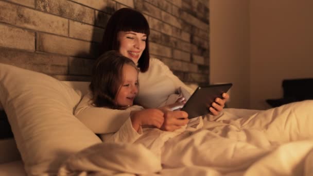 Matka i córka korzystające z tabletu, leżące w łóżku pod kocem i spędzające wieczór. — Wideo stockowe
