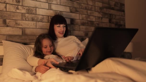 Уютная ночь прекрасная семья, мама и маленькая девочка, лежащие в постели и с помощью приложения на ноутбуке — стоковое видео
