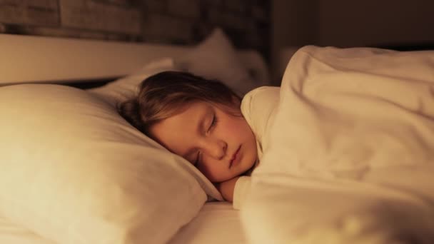 Oldalnézet nyugodt óvodás lány aludni kényelmes ágyban puha párnán. Édes álmok koncepciója — Stock videók