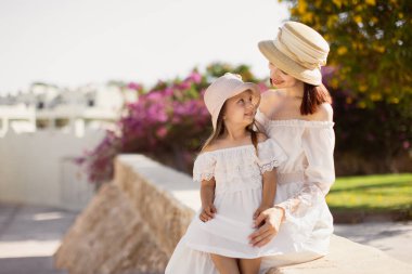 Hasır şapkayla poz veren kızıyla gülümseyen güzel bayan bulanık arka planda oturuyor..