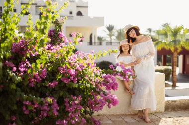 Beyaz elbiseli, saman şapkalı küçük kızıyla gülümseyen anne.