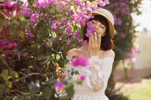 Jovem encantadora no belo jardim de flores em vestido branco e chapéu de palha — Fotografia de Stock