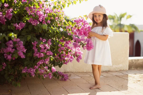 Menina bonita bonita com cabelo loiro longo em vestido branco e chapéu de palha desfrutando de primavera florescendo — Fotografia de Stock