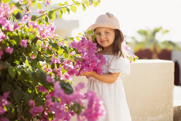 Menina bonita bonita com cabelo loiro longo em vestido branco e chapéu de palha desfrutando de primavera florescendo — Fotografia de Stock