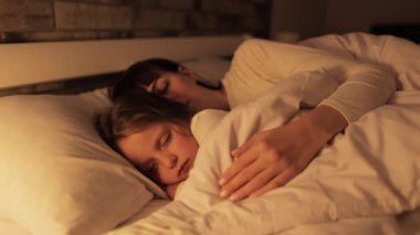 Genç anne ve küçük kızı yatakta birlikte uyuyorlar..