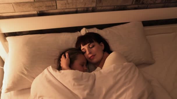 Kleines Mädchen liegt mit ihrer hübschen Mutter auf Kissen, umarmt und schläft zusammen im Bett — Stockvideo