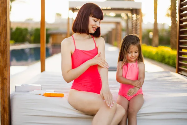 Une jeune maman et sa fille en maillot de bain rose appliquent de la crème ou de la crème solaire sur leurs mains — Photo