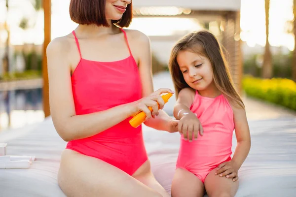 Gros plan de la jeune maman dans un maillot de bain rose pulvérisation SPF 50 crème de protection solaire sur sa main fille — Photo