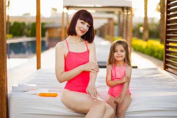 Une jeune maman et sa fille en maillot de bain rose appliquent de la crème ou de la crème solaire sur leurs mains — Photo