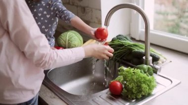 Genç, güzel, beyaz bir anne ve küçük tatlı kızının sebze yıkamasını yakından izleyin.