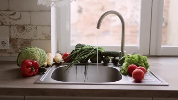 Le robinet est ouvert dans la cuisine légère près de la fenêtre afin que l'eau coule dans les légumes pour être soigneusement lavé. — Video