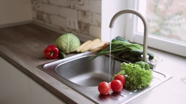 Il rubinetto viene aperto nella cucina luminosa vicino alla finestra in modo che l'acqua scorra nelle verdure da lavare accuratamente. — Video Stock
