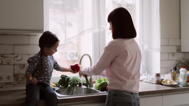 Liten flicka som hjälper sin muslimska mamma tvätta grönsaker i köket — Stockvideo