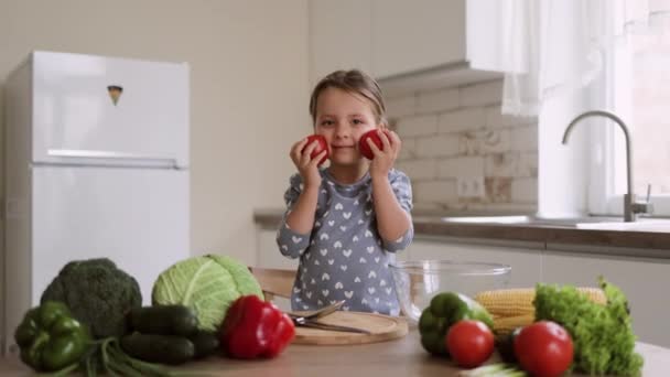 Chica sonriente con ropa casual sostiene tomates en sus manos mientras toca sus mejillas satisfechas de cocinar ensalada — Vídeos de Stock