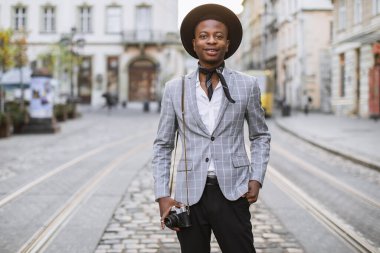 Eski fotoğraf makinesiyle sokakta poz veren Afrikalı bir adam.