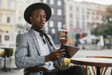 Afrikalı adam kahve içiyor ve kafede tablet kullanıyor.