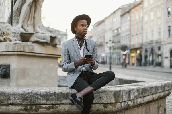 Afrikaanse Amerikaanse man zit buiten en met behulp van smartphone — Stockfoto