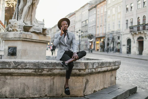 Afrikaanse man praten op mobiele terwijl zitten op straat — Stockfoto